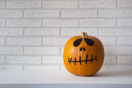 Halloween pumpkin with black eyes and mouth, with white brick background.	
の写真素材