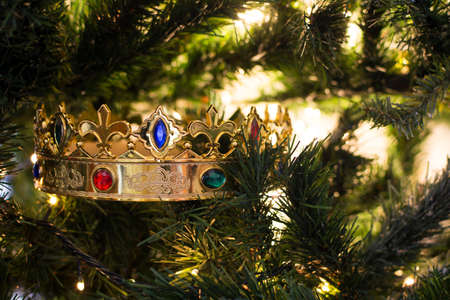 A golden wizard king crown with colored gems, among the branches of a Christmas tree illuminated by its Christmas lights.の写真素材