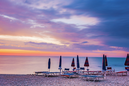 sunrise in a stony beach with umbrellas and sunbedsの写真素材