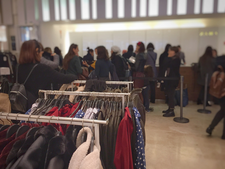 Rome, Italy, november 25, 2017: clothes in the hangers in a big white store with people in the...