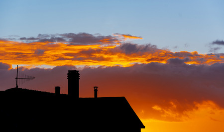silhouette of residential building with roofs and TV antenna receiver at sunsetの写真素材