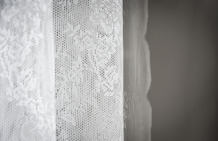 White curtain decorated with sewed floral pattern in lace. Interior shot with natural soft light