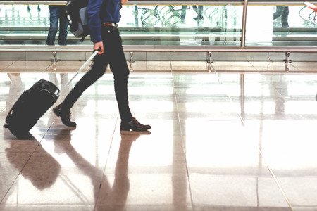 Traveler pulling suitcase in modern airport terminal. Travel and transportation concept