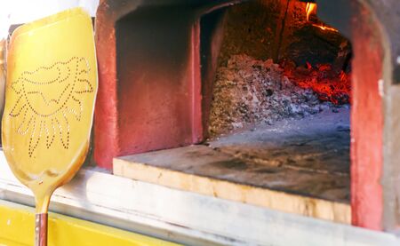 wood oven for baking pizza with ashes, burning embers and fire. Leaning against the oven there is a...