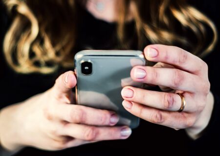 the hands of a young caucasian brunette woman while holding a smartphone typing on the touch screen....