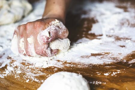 female hand kneading a flour dough by rolling it on a wooden board. Preparation of flour-based food such as bread or pizzaの写真素材