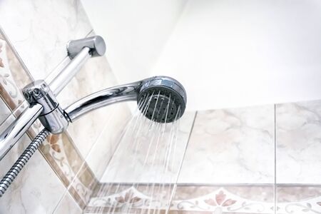 Interior of a shower with water flowing from the shower head. Droplets and moisture. Walls with decorated tiles. Hygiene and personal careの写真素材