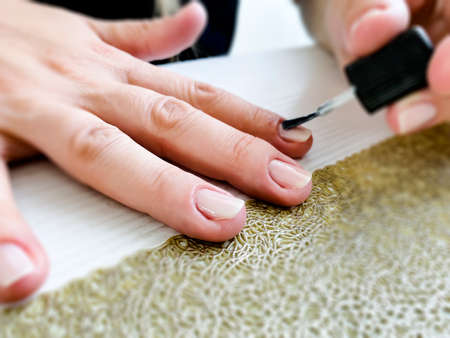 Hands of a female applying transparent nail polish on the nails with a black brush