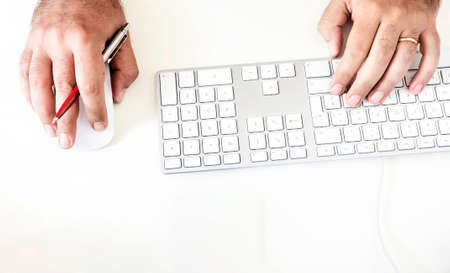 a male while using the computer keyboard and mouse holding out a red pen in his right hand....