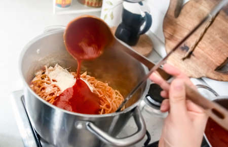 Seasoning a pan full of freshly cooked spaghetti by pouring the tomato sauce with a steel ladle....