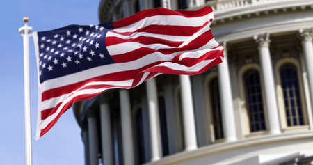 The flag of the united states of america flying in front of the capitol building blurred in the background. United states federal congress on Capitol hill in Washington D.C. Democracy and freedom.の写真素材