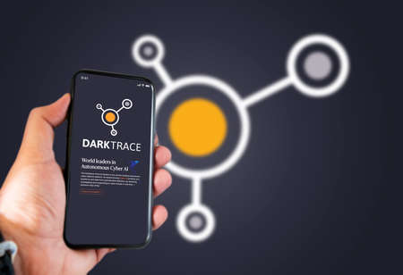 Cambridge, UK, May 2021: A hand holding a phone with the Darktrace company logo on the screen....