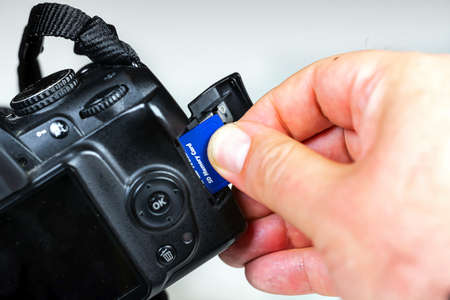 Photographer inserting or removing a blue memory card into the slot in the camera. Data storage and protection. Photographic equipment and technologyの写真素材