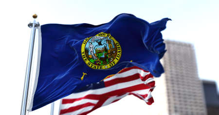 the flag of the US state of Idaho waving in the wind with the American stars and stripes flag blurred in the background. On July 3, 1890, Idaho became the 43rd state to join the Unionの写真素材