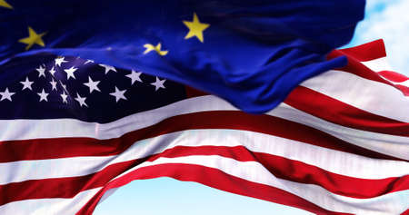 The national flag of the United states of America waving in the wind with the European Union flag blurred in the foreground. Politics and finance. Global finance, International relations and diplomacyの写真素材
