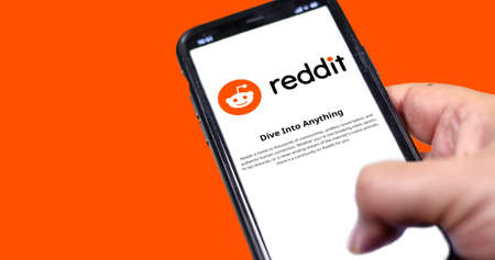 Rome, Italy, January 2022: Hand holding a smart phone with Reddit mobile app on the screen on an orange background. Reddit is an American social news aggregation and discussion website applicationのeditorial素材