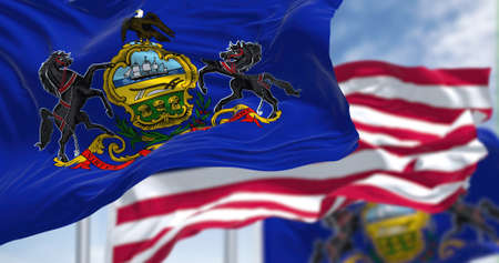 The Pennsylvania state flag waving along with the national flag of the United States of America. In the background there is a clear sky. Pennsylvania is a U.S. state in the northeastの写真素材