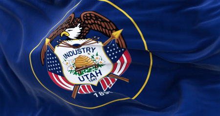 The Utah state flag fluttering in the wind. State seal surrounded by a golden circle on a dark blue...