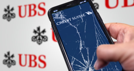 New York, US, March 2023: Hand holding a phone with Credit Suisse logo on cracked screen. UBS logo blurred on white background. UBS bought Credit Suisse for 3B CHF in stock. Illustrative editorialのeditorial素材