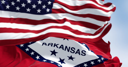 Arkansas state flags waving with the national flag of the United States of America on a clear day....