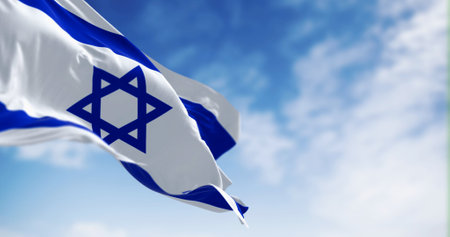 State of Israel national flag waving in the wind on a clear day. Blue Star of David in the center,...