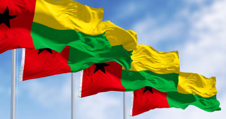 National flags of Guinea-Bissau waving in the wind on a clear day. Vertical red stripe, black star left, yellow and green horizontal stripes right. 3d illustration render. Fluttering fabricの写真素材