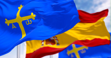 The Asturias flags waving with Spanish flag on a clear day. Autonomous community in northern Spain. Blue with golden victory cross. 3d illustration render. Rippling fabric. Selective focusの写真素材