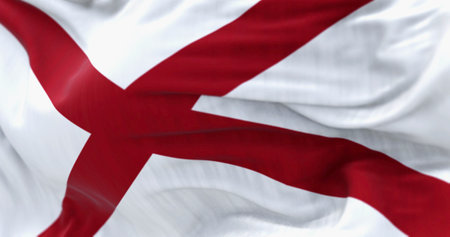 Close-up of Alabama state flag waving on a sunny day. The flag of Alabama features a red cross on a...