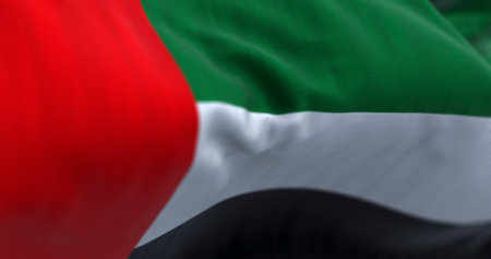 Close-up view of the United Arab Emirates national flag waving in the wind. The Emirates is a country in Western Asia. Rippled fabric. Textured background. Selective focus. Realistic 3d illustrationの写真素材