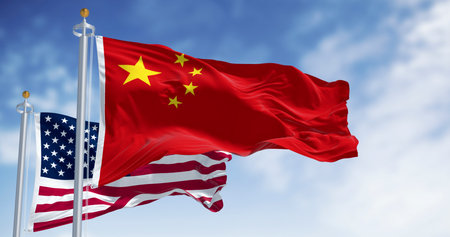 3D render of Chinese and American flags waving side by side in the wind, symbolizing diplomacy, patriotism and international relations under a clear sky.の写真素材