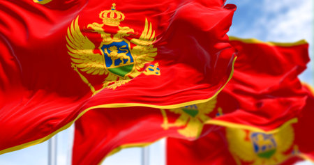 National flags of Montenegro waving in the wind on a clear day. Red with a golden border and...