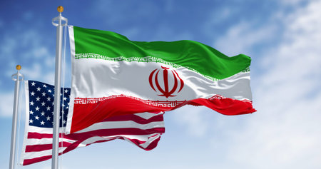 The national flags of Iran and the USA waving on a clear day. Symbolizing international relations,...