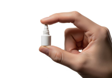 A close-up shot of a person's hand holding a miniature white nasal spray bottle. The background is pure white.の素材