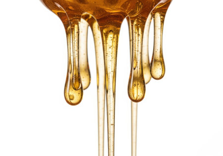 Viscous golden honey cascades down in thin streams and droplets against a clean white backdrop, showcasing its rich texture and color.の素材