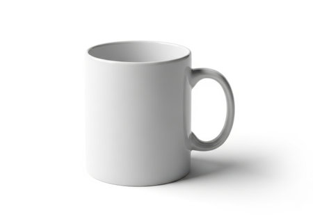 A simple white ceramic mug with a curved handle sits on a clean white surface, casting a subtle shadow.の素材