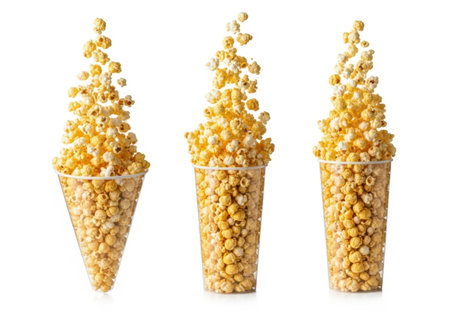 Three clear plastic cups are filled to the brim and overflowing with fluffy, golden popcorn against a white background.の素材