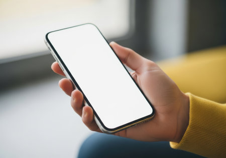 A person's hand holds a modern smartphone with a blank white screen, ready for content or interaction.の素材