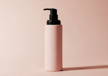 A tall, slender pink bottle with a black pump dispenser stands against a soft, gradient pink background.の素材