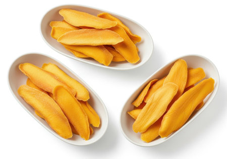 Three white oval dishes are filled with golden yellow, thin slices of dried mango, presented against a white background.の素材