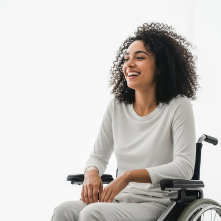 A young Black woman with curly hair sits in a wheelchair, laughing joyfully against a white background. She wears casual clothing.の素材