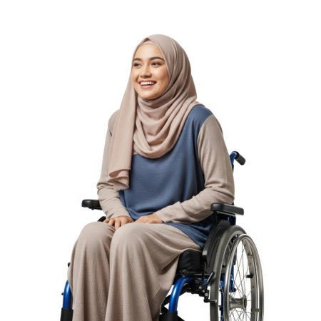 A young woman in a hijab and modest clothing smiles while sitting in a wheelchair against a plain white backdrop.の素材