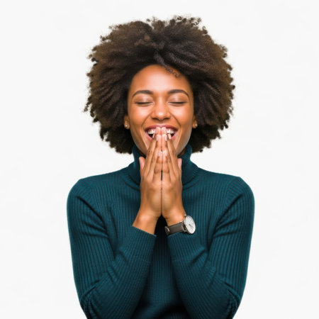 A Black woman with an afro laughs heartily, covering her mouth with her hands, eyes closed in delight against a white background.の素材