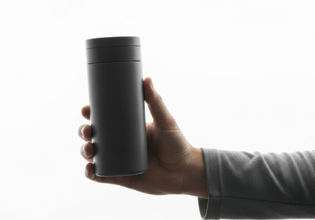 A person's hand and forearm are visible, holding a dark, tall, cylindrical object. The background is stark white.の素材