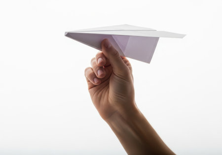 A close up of a person's hand holding a white paper airplane, ready to be thrown. Isolated on a white background.の素材