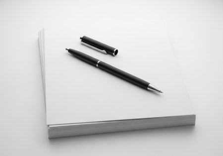 A sleek black pen and its cap lie on a clean, unwritten white notebook page.の素材