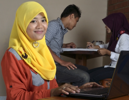 Young Muslim female student with laptop smiling while two friends discussing in the backgroundの写真素材