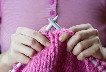 Close up of a female hands knitting pink woolen threads