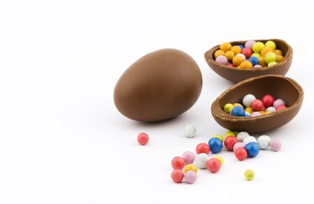 Closeup view of group chocolate eggs full of colorful sweet dragee on white background