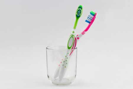 Green and pink toothbrushes in glass cup isolated on grey backgroundの写真素材