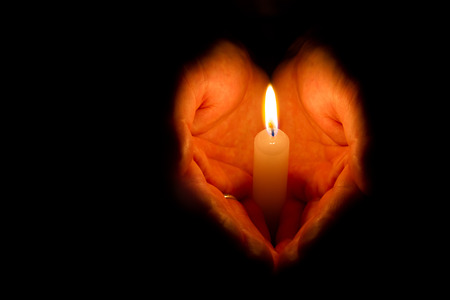 Man hands holding a burning candle on dark backgroundの写真素材